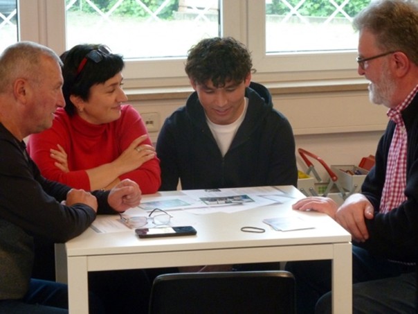 Drei Erwachsene und ein Junge an einem Tisch, Deutschwerkstatt-Huckepack e.V.